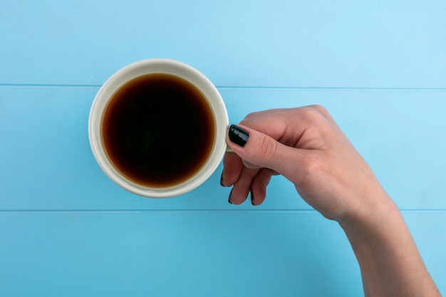 Vue de dessus des mains de femme tenant une tasse de thé sur fond bleu