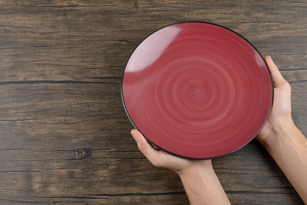 Vue de dessus des mains de l'homme tenant une assiette rouge vide sur une table en bois.