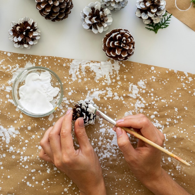 Photo gratuite vue de dessus des mains peignant des pommes de pin pour noël