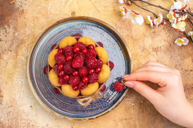 Vue de dessus des mains tenant une fraise sur un gâteau moelleux fraîchement cuit avec des fruits sur table de couleurs mixtes