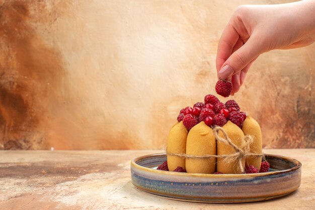 Vue de dessus des mains tenant une fraise sur un gâteau moelleux fraîchement cuit avec des fruits sur table de couleurs mixtes