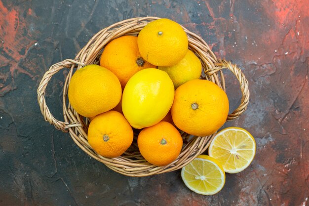 Vue de dessus des mandarines fraîches dans un panier en osier, des citrons coupés sur un sol rouge foncé