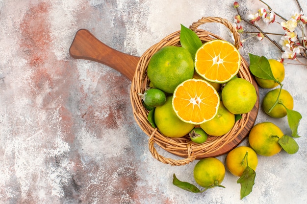 Photo gratuite vue de dessus des mandarines fraîches dans un panier en osier sur une planche à découper une branche de fleur d'abricot sur fond nu