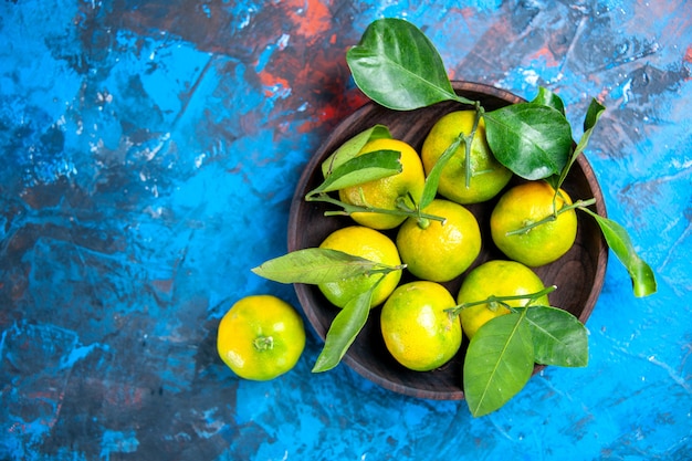 Photo gratuite vue de dessus mandarines jaunes avec des feuilles dans un bol en bois sur l'espace libre de surface bleue