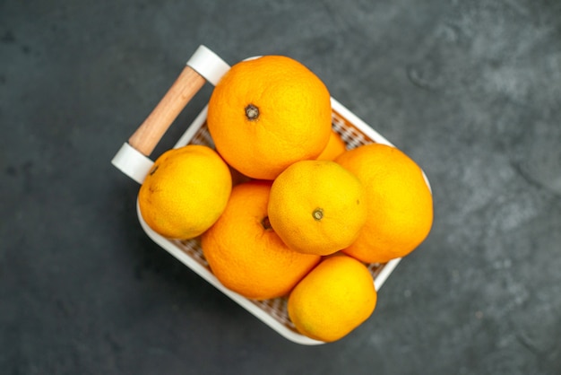 Vue de dessus des mandarines et des oranges dans un panier en plastique sur une surface sombre