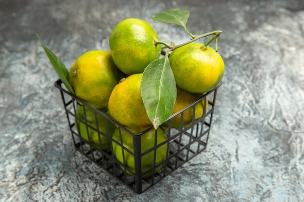 Vue de dessus des mandarines vertes avec des feuilles dans un panier sur fond gris