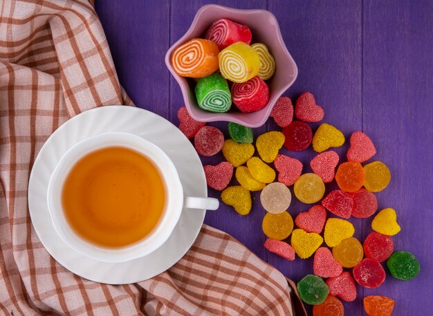 Vue de dessus des marmelades et tasse de thé sur soucoupe sur tissu à carreaux et fond violet