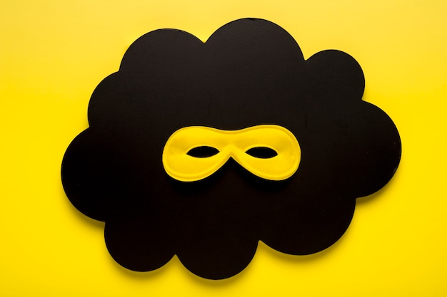 Vue de dessus masque de carnaval jaune sur nuage de papier noir