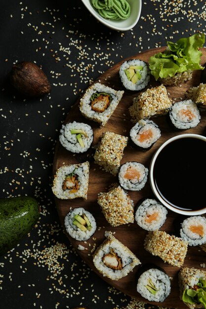 Vue de dessus mélanger des rouleaux avec de la sauce soja sur un support avec des graines de sésame, du riz au gingembre et du wasabi