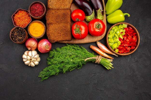 Vue de dessus des miches de pain noir avec assaisonnements verts et légumes sur fond sombre plat salade repas santé