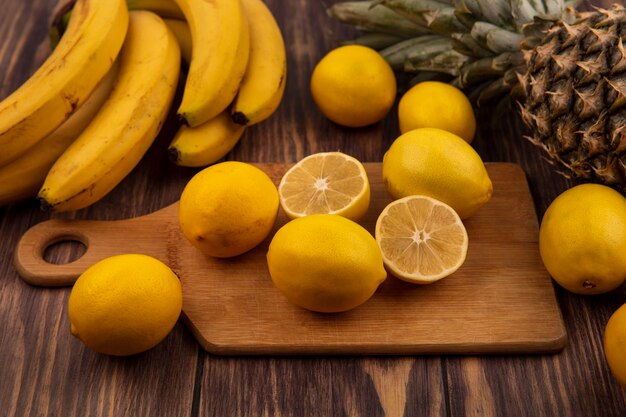 Vue de dessus de la moitié des agrumes et des citrons entiers sur une planche de cuisine en bois avec ananas et bananes isolé sur une surface en bois