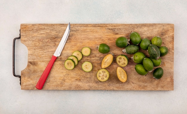 Photo gratuite vue de dessus de la moitié et des feijoas frais entiers isolés sur une planche de cuisine en bois avec un couteau sur une surface grise