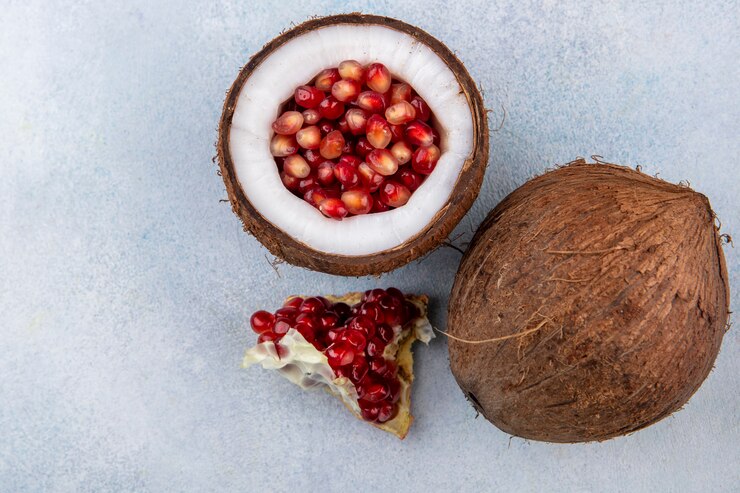 Photo gratuit vue de dessus de la moitié de la noix de coco à l'intérieur des graines de grenade avec noix de coco et tranche de grenade sur une surface blanche