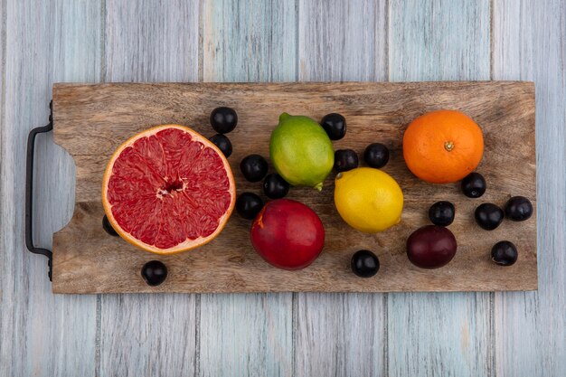 Vue de dessus la moitié de pamplemousse avec citron vert orange et pêche avec prune cerise sur une planche à découper