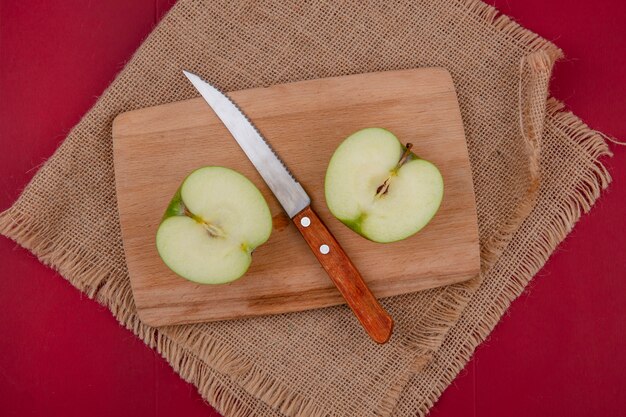 Vue de dessus de la moitié de la pomme coupée avec un couteau sur une planche à découper sur un sac sur une surface rouge