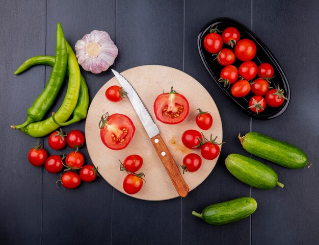 Vue de dessus de la moitié de la tomate coupée et du couteau sur une planche à découper avec de l'ail tomate poivrée sur une surface noire