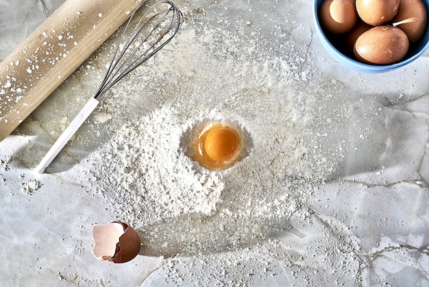 Vue de dessus d'un monticule de plancher avec un œuf, un batteur et un rouleau à pâtisserie en bois