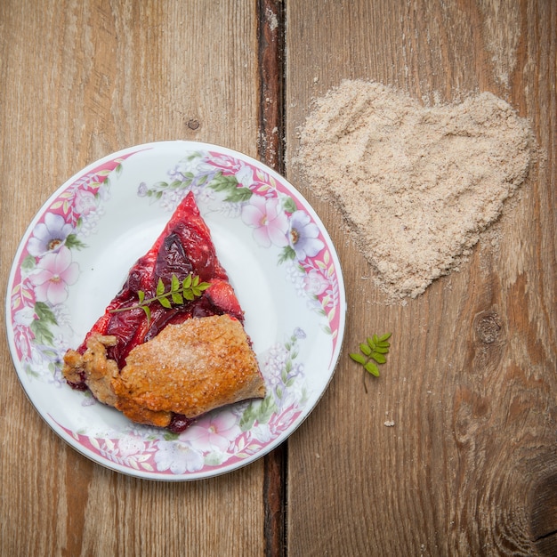 Vue de dessus un morceau de tarte aux fraises avec des miettes de noix et un cœur dans une assiette à fleurs ronde