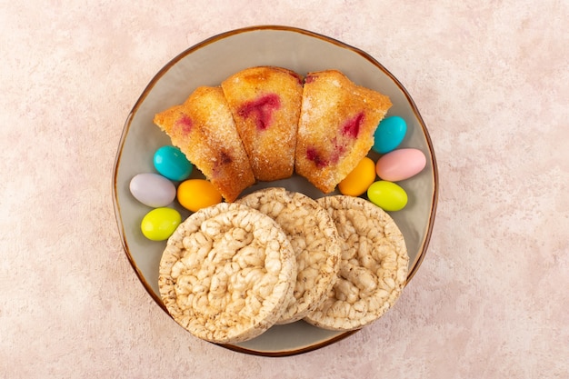 Une vue de dessus des morceaux de gâteau aux cerises avec des bonbons et des biscuits sur le bureau rose gâteau biscuit sucre sucré