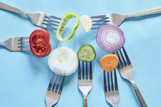 Vue de dessus de morceaux de légumes frais et d'épices sur des fourchettes contre une surface bleue