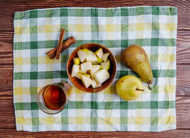 Photo gratuite vue de dessus des morceaux de poire dans un bol en bois avec un verre de limonade et des bâtons de cannelle sur une nappe à carreaux