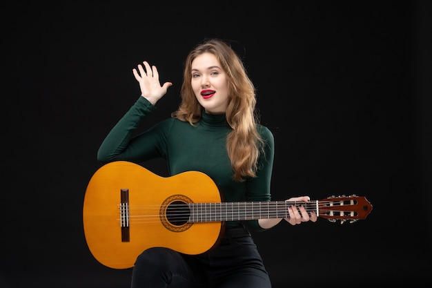 Vue de dessus d'une musicienne heureuse tenant une guitare et montrant cinq dans l'obscurité