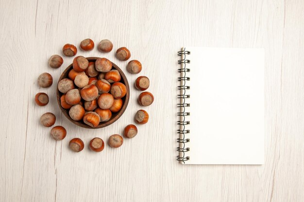 Vue de dessus des noisettes fraîches avec bloc-notes sur un bureau blanc casse-croûte de noix de noix