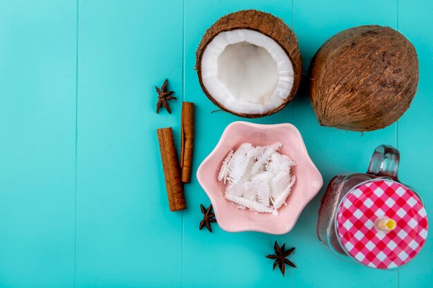 Vue de dessus des noix de coco brunes avec des pulpes de noix de coco dans un bol rose avec du jus de cannelle dans un bocal en verre sur bleu