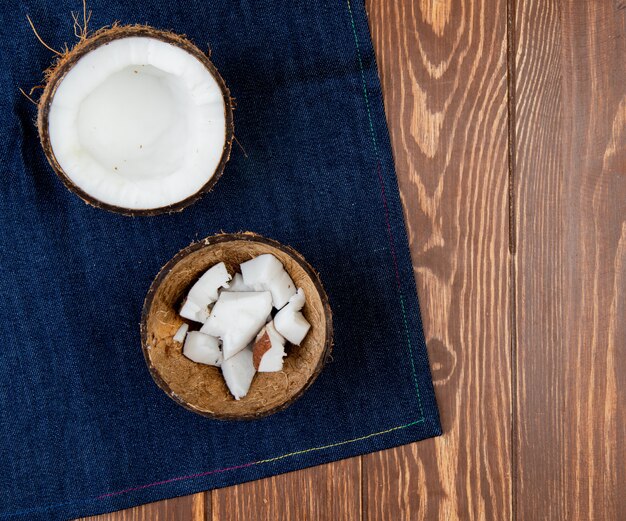 Vue de dessus de la noix de coco à moitié coupée avec des tranches de noix de coco en coque sur un tissu de jeans et un fond en bois avec copie espace