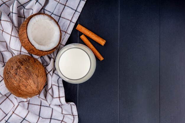 Vue de dessus des noix de coco avec un verre de lait avec des bâtons de cannelle sur nappe à carreaux sur fond noir avec copie espace