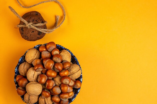 Vue de dessus des noix entières et des noisettes dans un bol et des biscuits à l'avoine attachés avec une corde sur jaune