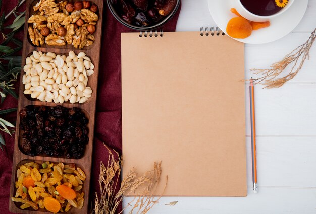 Vue de dessus des noix mélangées et des fruits secs dans une boîte en bois et un carnet de croquis sur rustique