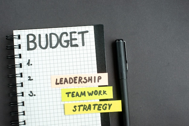 Vue de dessus note de budget dans le bloc-notes avec un stylo sur la stratégie de surface sombre marketing d'entreprise travail d'équipe bureau leadership succès de l'emploi