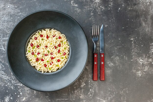 Vue de dessus des nouilles ramen asiatiques sur une fourchette et un couteau à assiette ronde noire sur un espace libre de table sombre