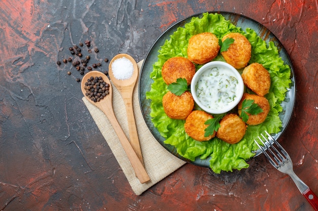 Photo gratuite vue de dessus nuggets de poulet fourchette sur assiette sel et poivre noir dans des cuillères en bois sur table sombre