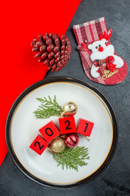 Vue de dessus des numéros d'accessoires de décoration sur une assiette et un cône de conifère chaussette de Noël sur une table sombre