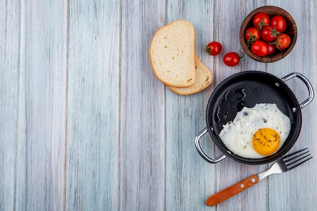 Vue de dessus de l'oeuf au plat dans le moule avec une fourchette et un bol de tranches de tomate et de pain sur bois avec copie espace