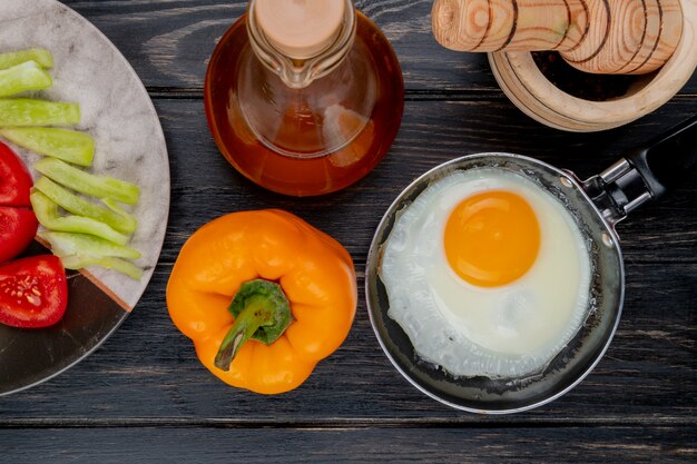 Vue de dessus de l'oeuf au plat sur une poêle avec un piment d'orang avec du vinaigre de pomme sur un fond en bois