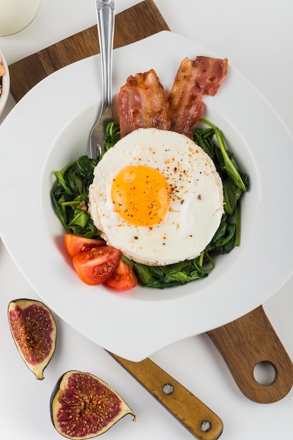 Photo gratuite une vue de dessus d'oeuf avec du bacon; figue; épinards et tomates sur une plaque blanche sur fond blanc