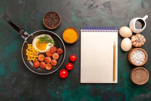 Photo gratuite vue de dessus des œufs brouillés avec des saucisses et différents assaisonnements sur un bureau vert foncé