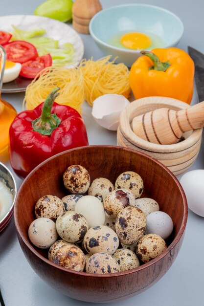 Vue de dessus des oeufs de caille sur un bol en bois avec des poivrons colorés sur fond blanc