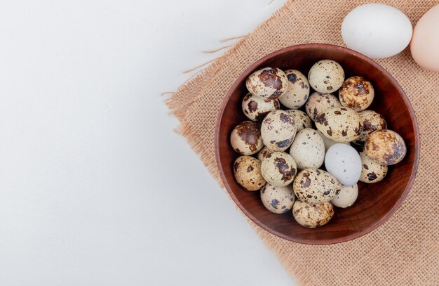 Vue de dessus des oeufs de caille sur un bol en bois sur tissu sac avec des oeufs de poule sur fond blanc