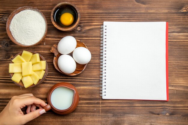 Vue de dessus des œufs crus avec de la farine de fromage et du lait sur le produit de surface en bois pâte aux œufs repas crus