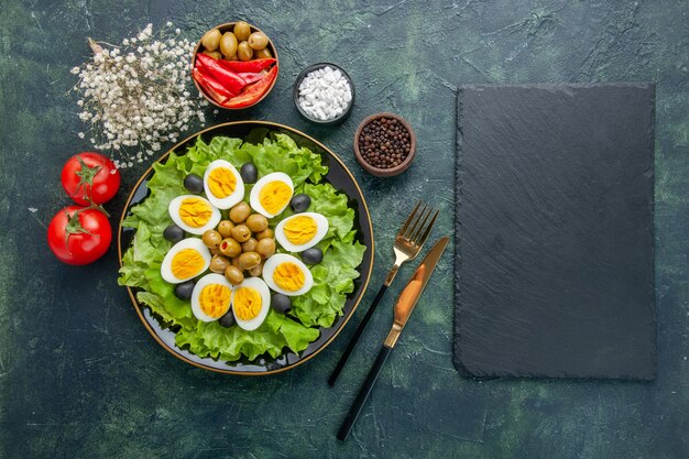 Vue de dessus des œufs durs en tranches avec salade verte et olives sur fond bleu foncé