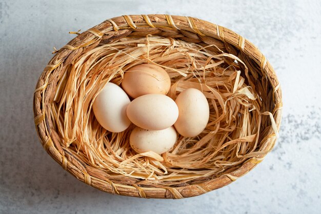 Vue de dessus des œufs de poule bio dans un panier sur une surface grise.