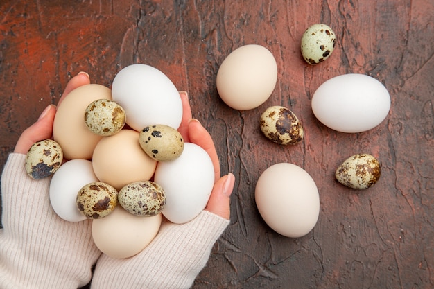 Vue de dessus des œufs de poule blancs dans les mains des femmes sur la table sombre