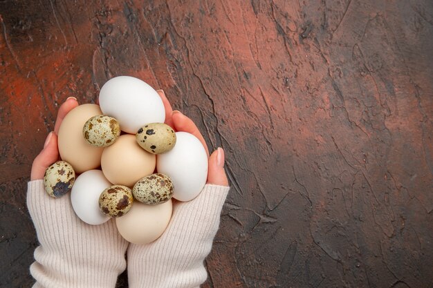 Vue de dessus des œufs de poule blancs dans les mains des femmes sur la table sombre