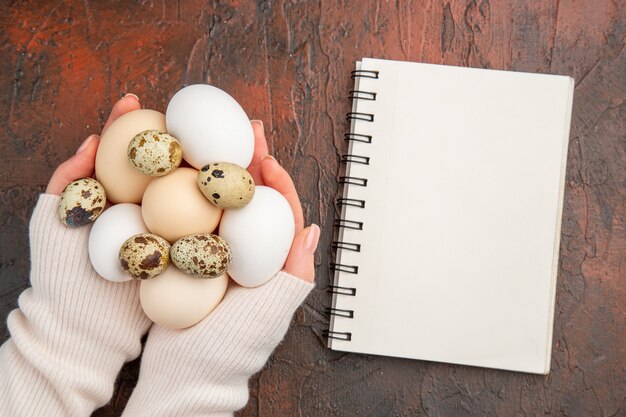 Vue de dessus des œufs de poule blancs dans les mains des femmes sur la table sombre