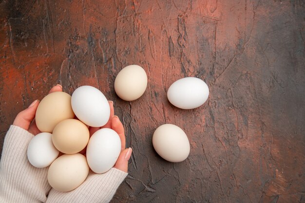 Vue de dessus des œufs de poule blancs dans les mains des femmes sur la table sombre