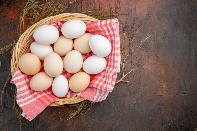 Vue de dessus des œufs de poule blancs à l'intérieur du panier avec une serviette sur la table sombre
